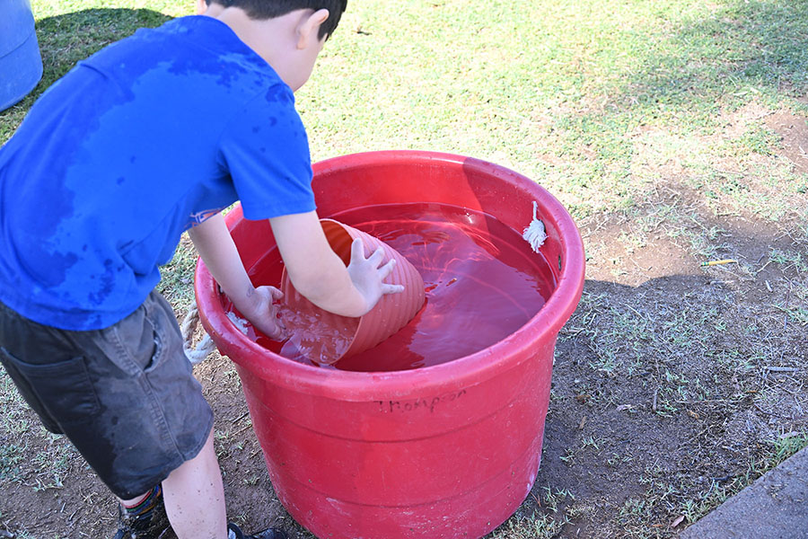 A boy puts a small bucket into a larger bucket of water