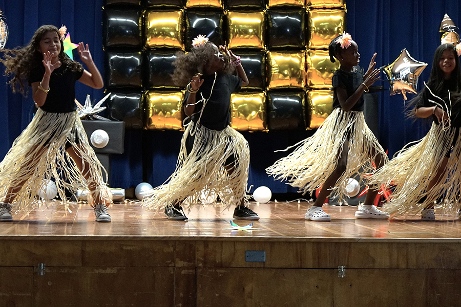 A group of girls dance on stage in long grass skirts