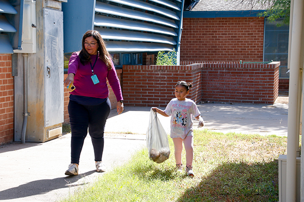 A little girl and a woman pick up trash outside