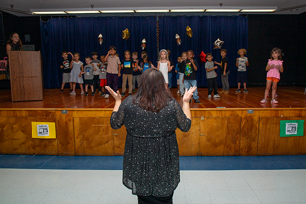 A teacher directs her students on stage as they perform